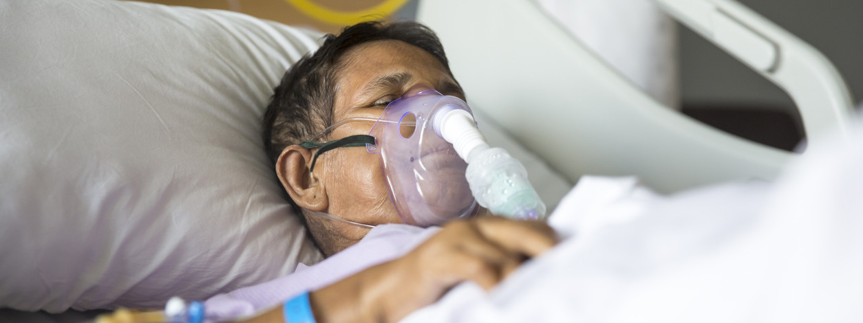 Old woman patient lying on Hospital bed with ventilator mask on her nose. She has her eyes closed.