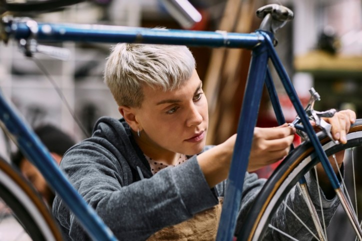 Eine etwa 20-jährige Frau justiert konzentriert ein Bauteil am Hinterrad eines Fahrrads. Sie arbeitet in einer Fahrradwerkstatt.