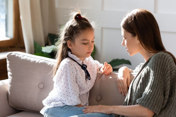 Eine Mutter spricht mit ihrer etwa 10 jährigen Tochter. Beide sitzen auf einem Sofa und schauen besorgt aus.