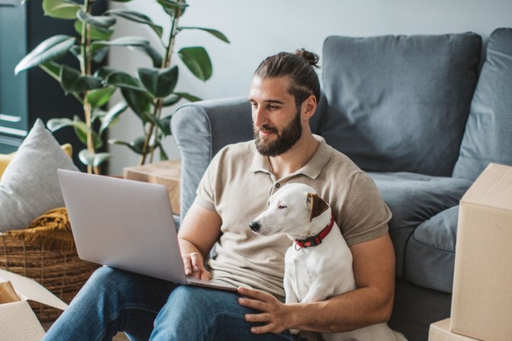 Ein etwa 30-jähriger Mann sitzt mit seinem Hund vor dem Laptop und scrollt durch die Online-Portale der AOK Sachsen-Anhalt.