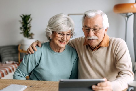 Ein älteres Paar sitzt am Tisch vor einem Tablet und schaut sich den AOK Online Coach an.