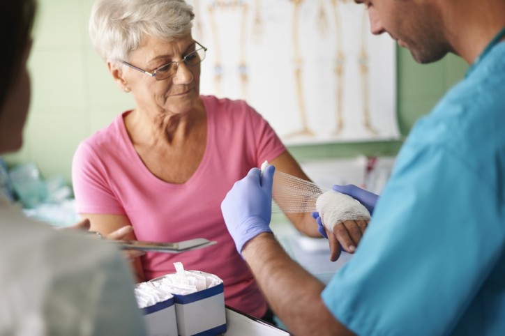 Eine Seniorin lässt sich von einem Arzthelfer nach einem Grillunfall die Hand verbinden.