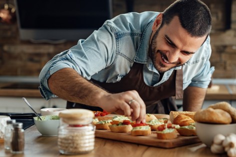 Ein etwa 35-jähriger Mann belegt Baguettescheiben mit Gemüse.