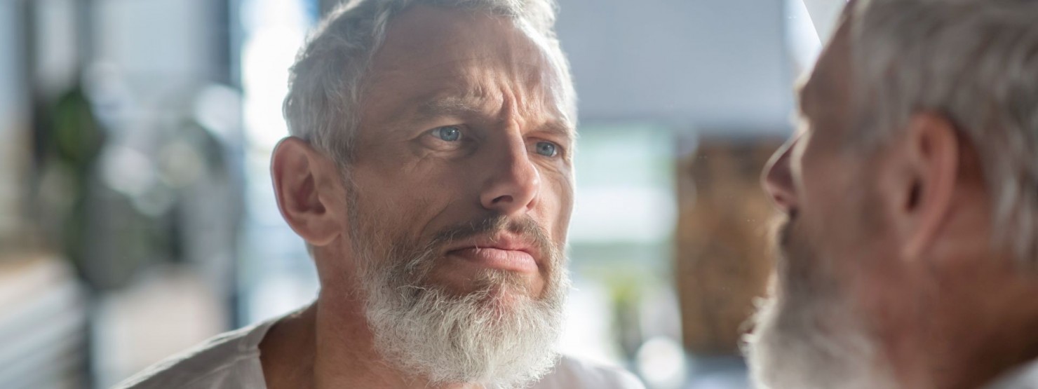 Ein Mann schaut sein Gesicht im Spiegel an und untersucht es auf Rosazea.