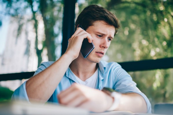 Ein etwa 30 jähriger Mann sitzt an einem Tisch und telefoniert mit einem Handy am rechten Ohr. Er schaut dabei sehr besorgt.