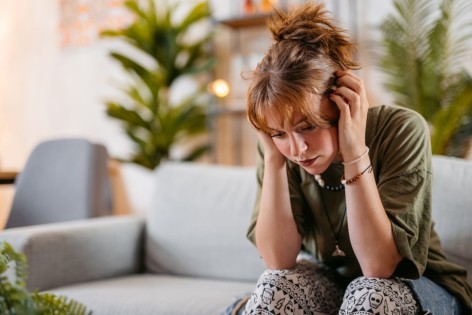 Eine junge Frau mit Depression sitzt auf der Couch und schaut traurig.