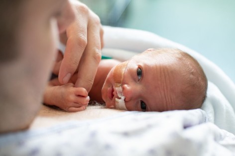 Ein zu früh geborenes Baby liegt auf der Brust seines Vates.