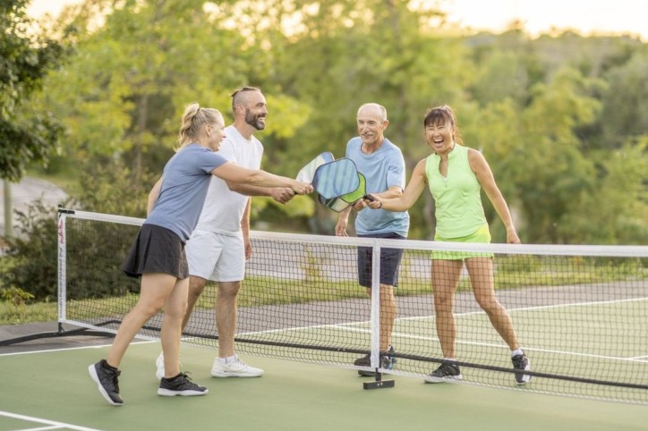 Eine Gruppe aus vier Erwachsenen Personen bestreiten ein Pickleball-Match.