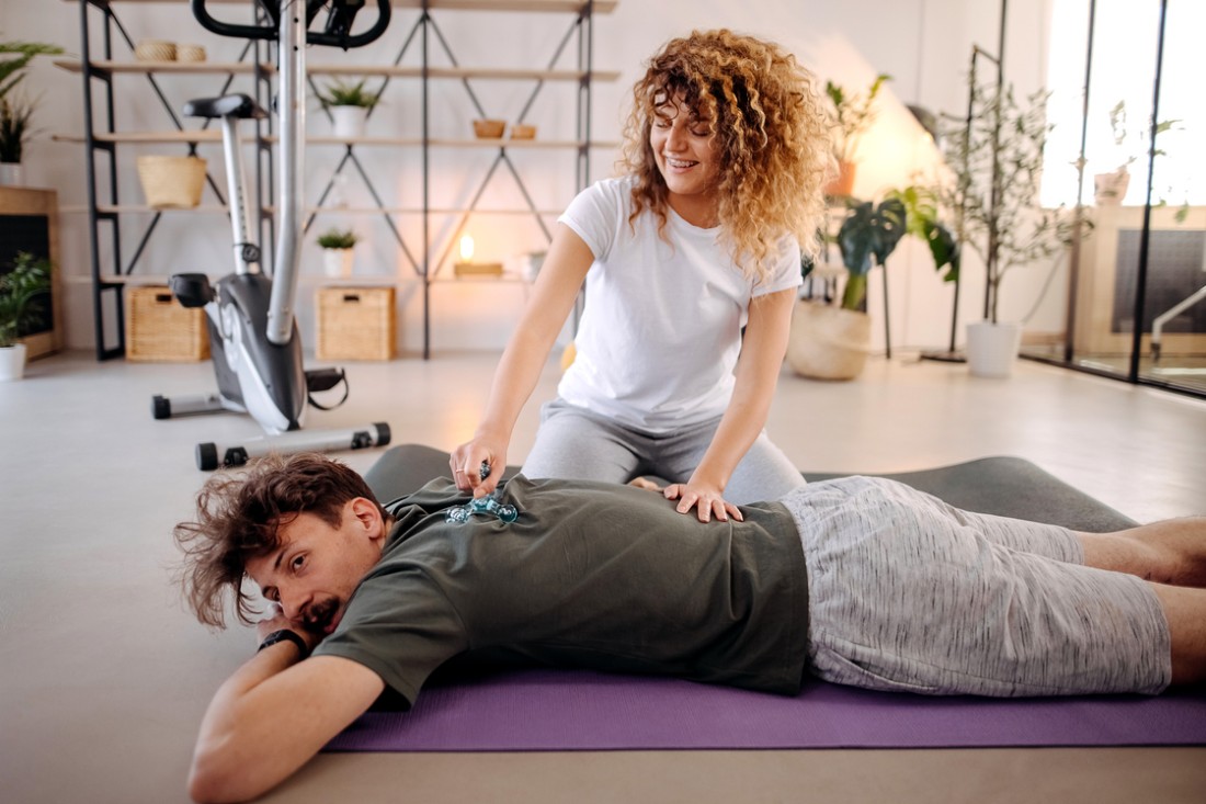 Eine Frau führt eine Akupressur an dem Rücken eines Mannes mit einem Massageknauf durch.