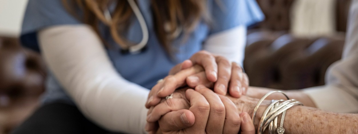 Freiwillige Helferin im Hospizdienst hält Hand einer Patientin