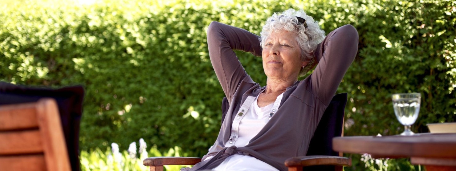 Eine Seniorin liegt im Garten auf einem Gartenstuhl mit verschränkten Armen.