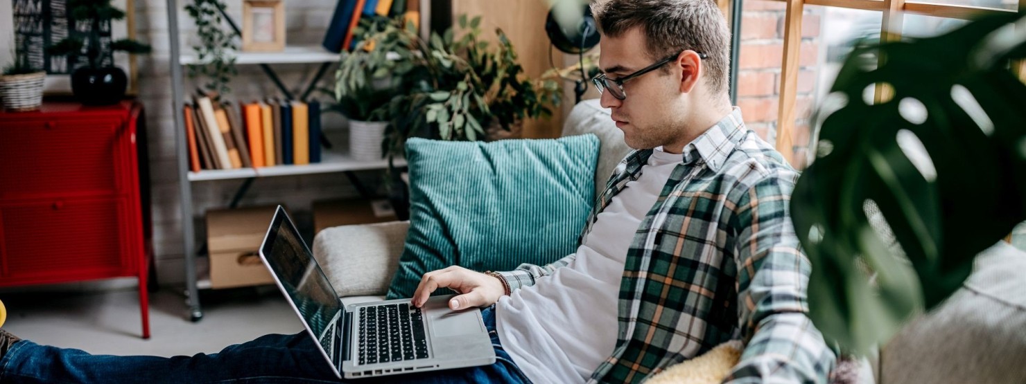 Handsome young man looking at laptop and smiling while lying on the sofa at home