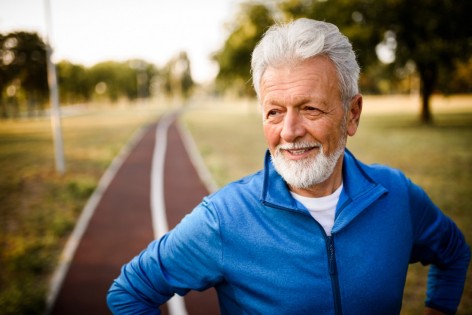 Ein glücklich schauender Senior macht beim Joggen eine Pause.