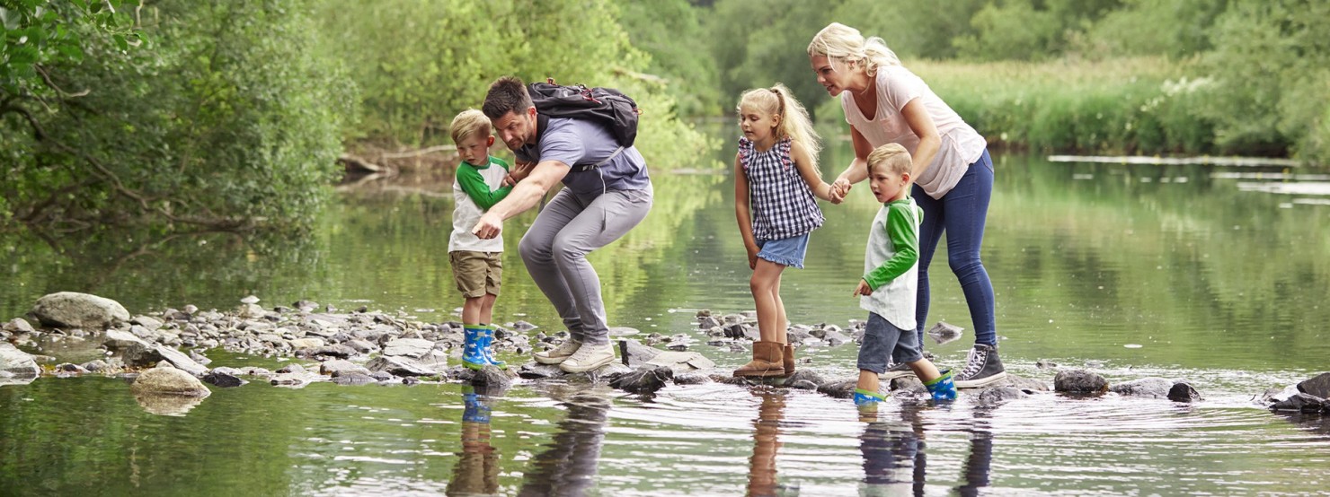 Mutter und Vater überqueren mit ihrer Tochter und zwei Söhnen einen Fluss im Wald.