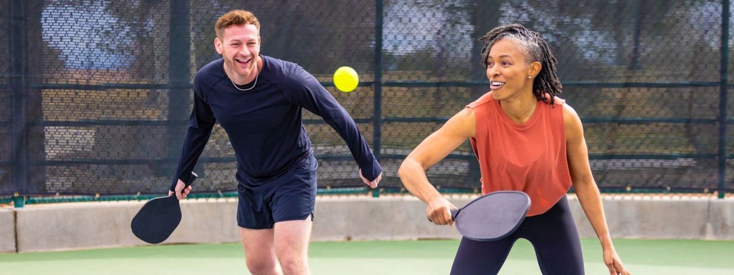 Ein junger Mann und eine junge Frau spielen als Team ein Pickleball-Doppel.