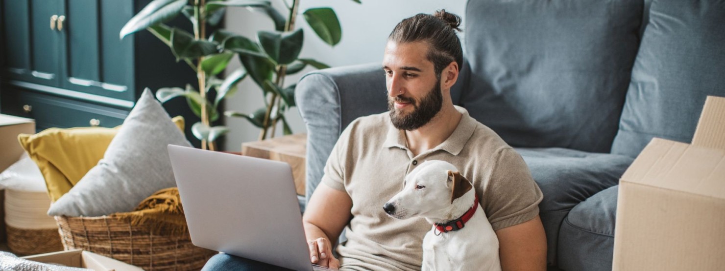 Ein etwa 30-jähriger Mann sitzt mit seinem Hund vor dem Laptop und scrollt durch die Online-Portale der AOK Sachsen-Anhalt.