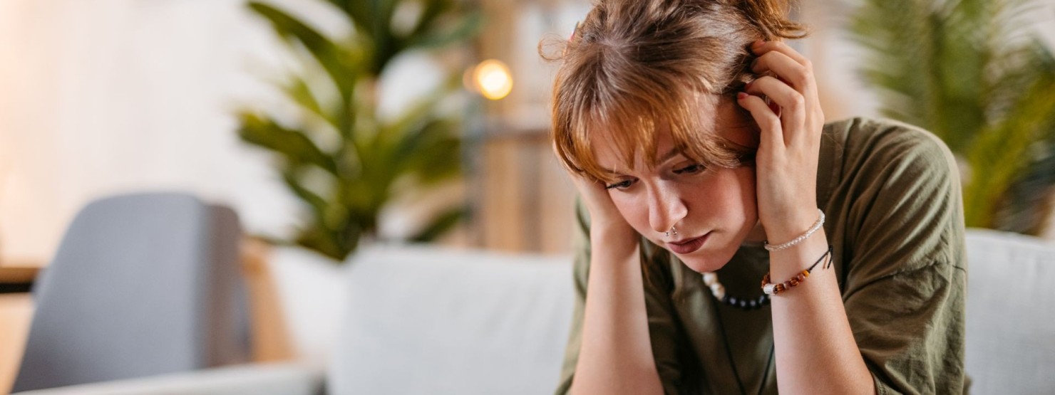 Eine junge Frau mit Depression sitzt auf der Couch und schaut traurig.