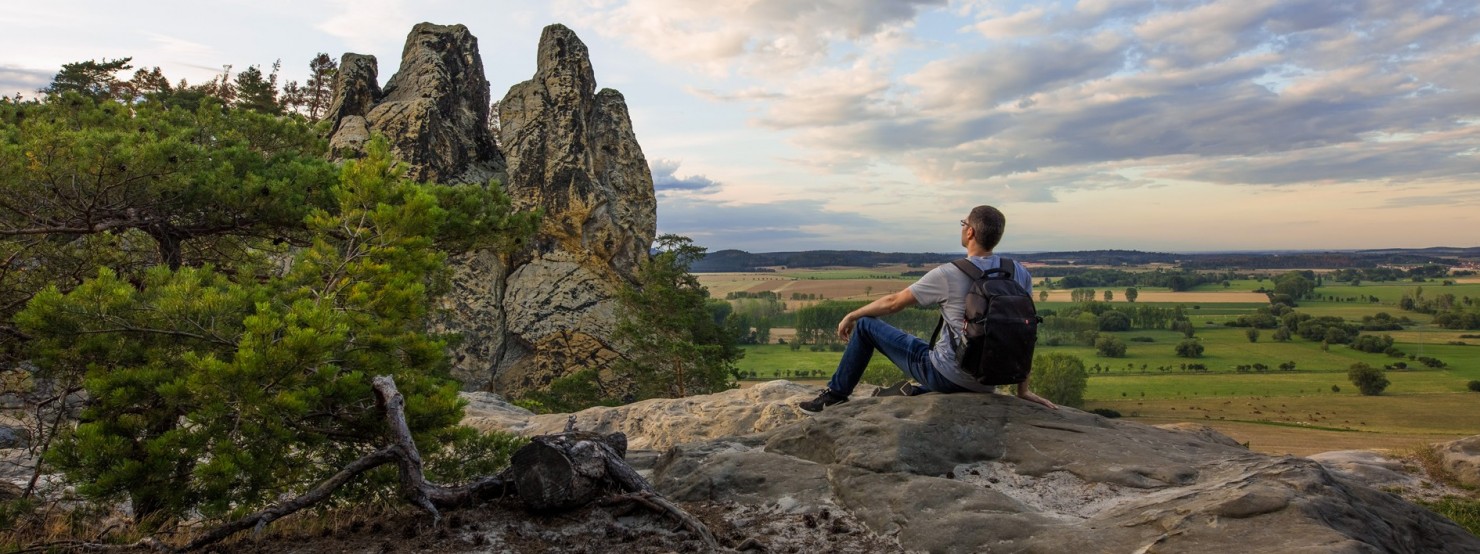 Mann mit Rucksack sitzt auf einem Felsen vor der Teufelsmauer.