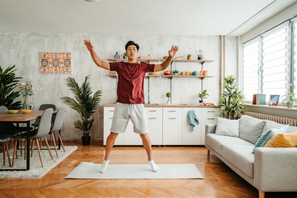 Ein etwa 30-jähriger Mann macht ein Cardio-Training auf einer Sportmatte im Wohnzimmer.