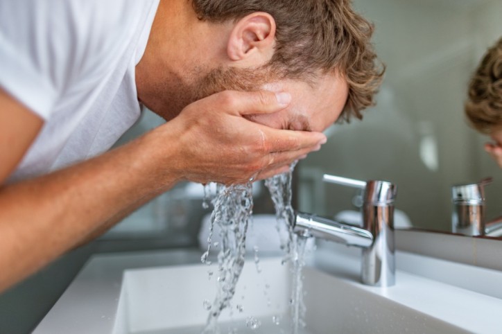 Ein Mann wäscht sich sein Gesicht mit klarem Wasser.