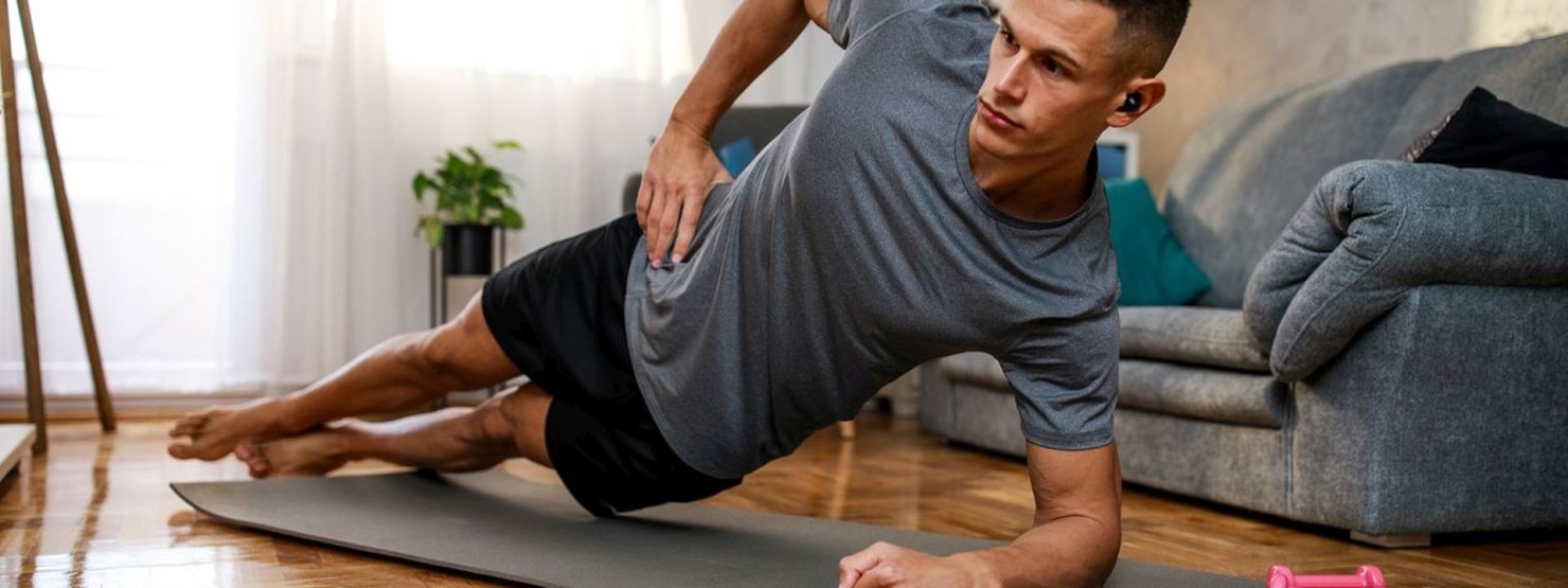 Junger Mann macht seitlichen Plank im Wohnzimmer.