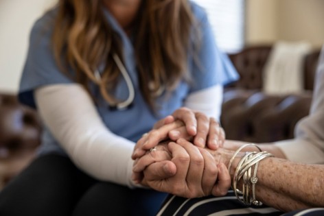 Freiwillige Helferin im Hospizdienst hält Hand einer Patientin