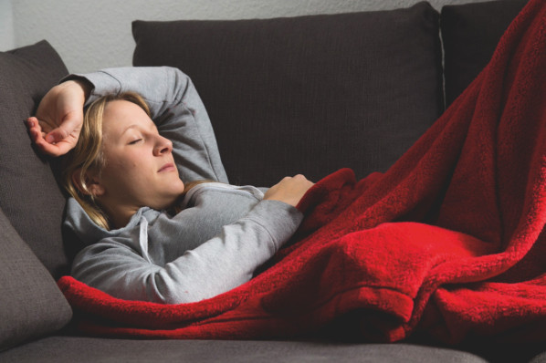 Eine erkältete Frau liegt auf der Couch und schläft