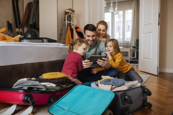 Junge Eltern mit zwei kleinen Kindern packen ihren Koffer für den Urlaub