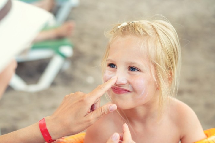 Ein Kind wird mit kindgerechtem Sonnenschutz aus der Urlaubsapotheke eingecremt