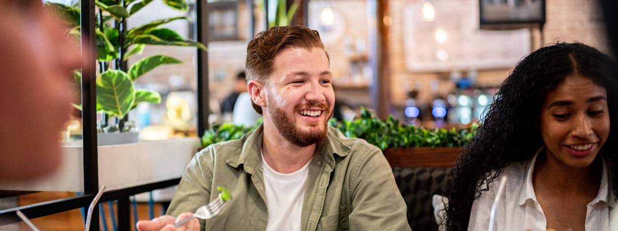 Ein lachender Mann mit Augenringen beim gemeinsamen Essen mit Freunden