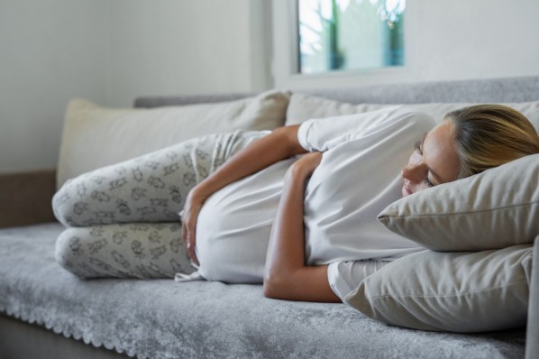 Eine schwangere Frau liegt mit Geburtswehen auf dem Sofa.