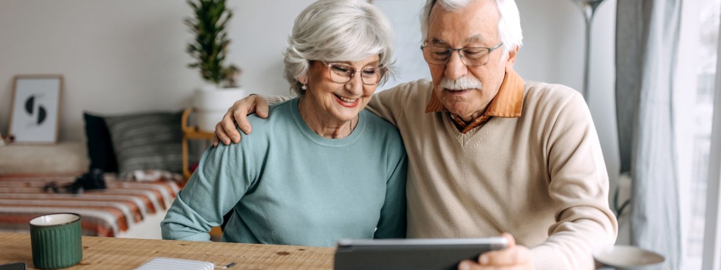 Ein älteres Paar sitzt am Tisch vor einem Tablet und schaut sich den AOK Online Coach an.