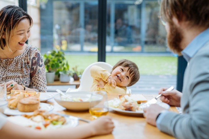 Eine Familie sitzt mit ihrem Baby am Essenstisch. Alle lachen gemeinsam.