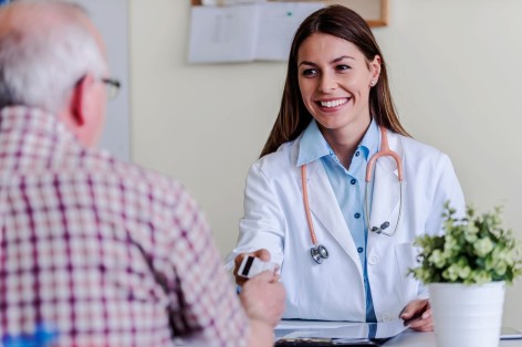 Ein Ärztin gibt einen älteren Patienten seine Versichertenkarte zurück. Dabei lächelt sie ihn an.