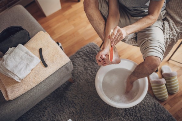 Man having foot bath at home and removing dead skin from feet