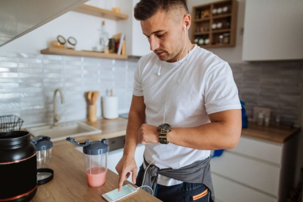 Junger Mann steht in der Küche und prüft seinen Fitnesstracker.