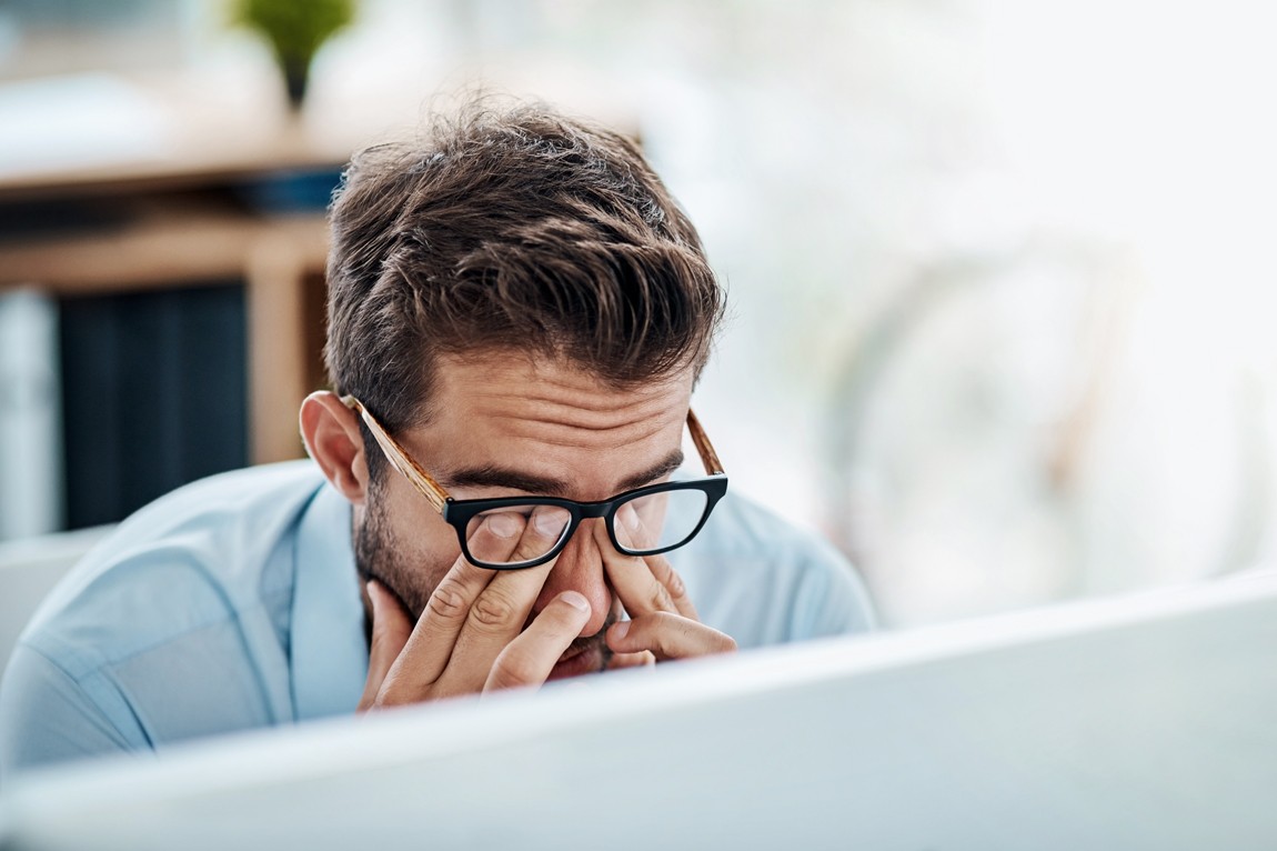 Ein etwa 35-jähriger Mann reibt sich erschöpft die Augen. Er sitzt vor einem Computer.